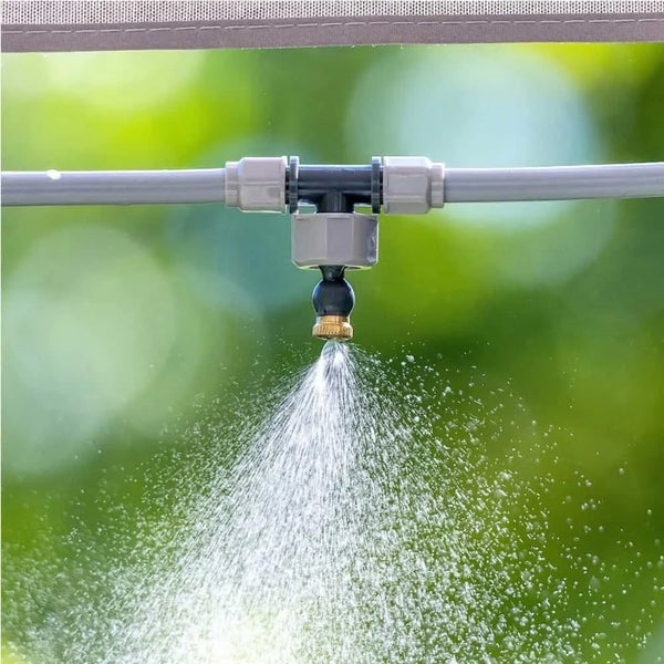 Ein T-Stück mit Sprühdüse als Teil eines Bewässerungssystems versprüht Wasser im Freien.