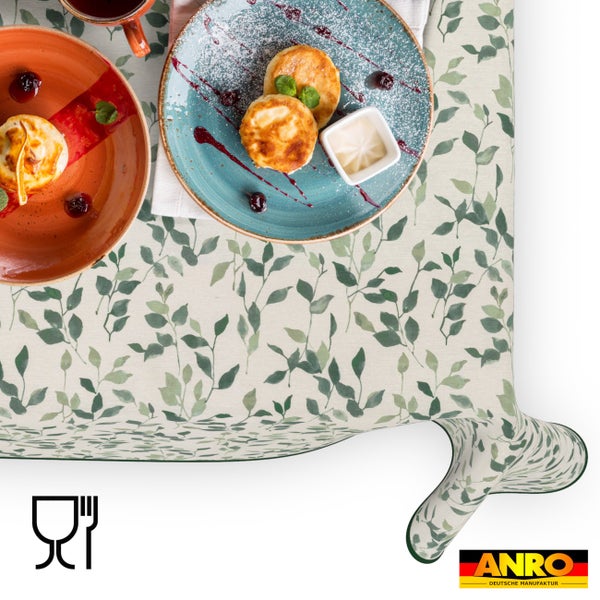 Abwaschbare Tischdecke mit grünem Blättermuster, eingedeckt mit Frühstückstellern, ANRO Deutsche Manufaktur Logo und lebensmittelecht Symbol.