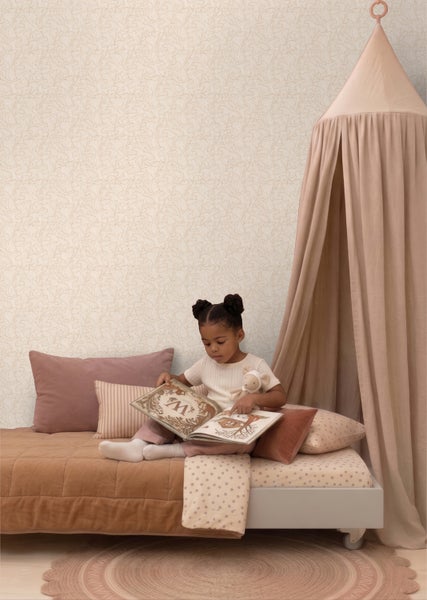 Helles Kinderzimmer mit dezent gemusterter Vliestapete, einem Bett mit verschiedenen Kissen und einem dekorativen Betthimmel.