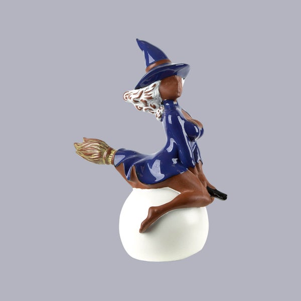 Dekorative Halloween-Figur einer Hexe mit blauem Hut und Kleid auf einem Besen reitend auf einer weißen Kugel.
