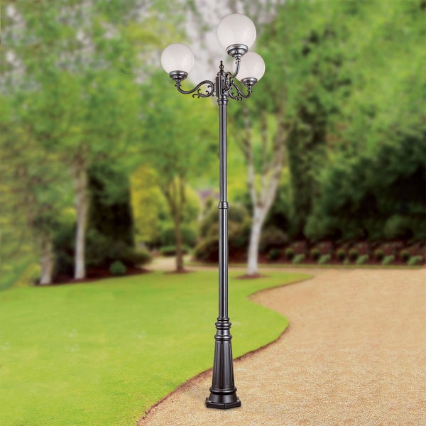 Klassische dreiflammige Mastleuchte mit weißen Kugelschirmen auf einem verzierten Metallmast in einer Gartenanlage.