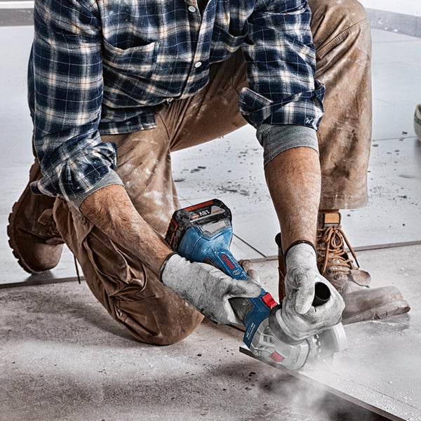 Handwerker kniet und schneidet eine Fliese mit einem Akku-Winkelschleifer