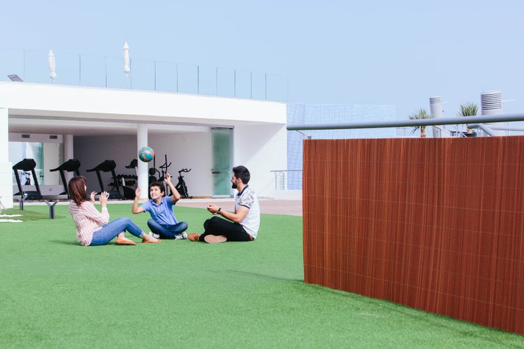 Szene im Freien mit Familie auf Kunstrasen, Ball spielend, mit einem Sichtschutzzaun im Vordergrund