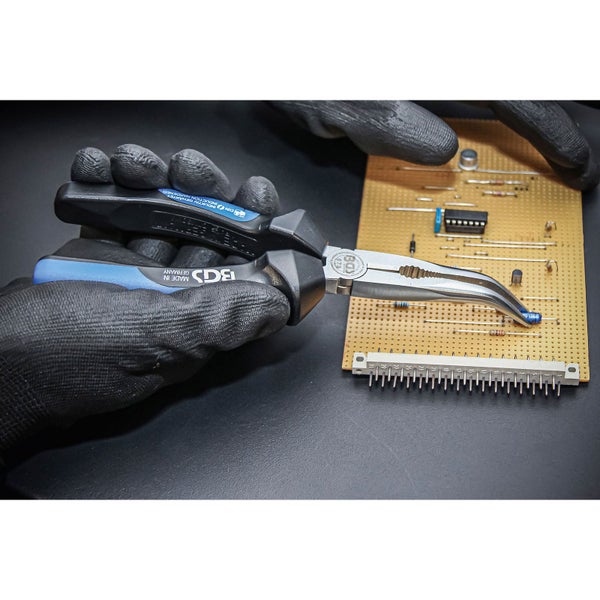 G gebogene Elektronikzange in der Hand mit Elektronikplatine im Hintergrund