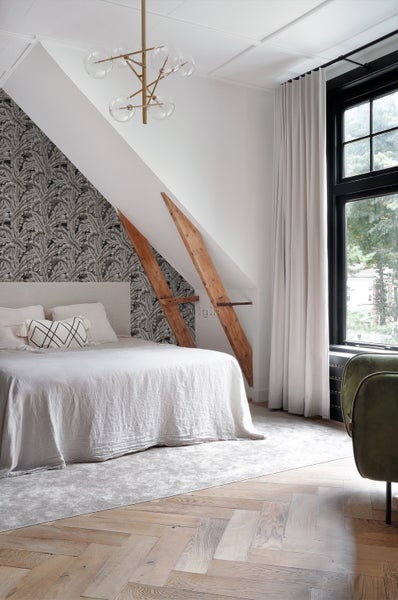 Schlafzimmer mit Bett, floraler Tapete, Holzregalen und einem modernen Kronleuchter