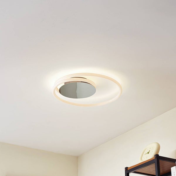 Moderne LED-Deckenleuchte mit zwei verschlungenen Leuchtringen und Spiegelfläche in einem hellen Raum.