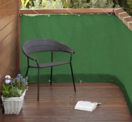 Grüner Balkon-Sichtschutz aus Stoff mit Metallösen, montiert an einem Balkon mit Holzboden und einem Sessel.