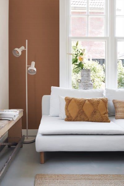 Wohnzimmer mit weißem Sofa, Zierkissen, Stehlampe und brauner Tapete