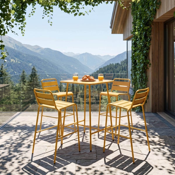 Modernes Set aus quadratischem Stehtisch und vier Barhockern auf einer hellen Terrasse mit Bergblick und Steinplatten.