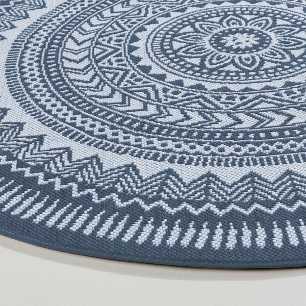 Detailansicht eines runden blau-weißen Teppichs mit geometrischem Mandala-Muster und Flachgewebe-Struktur.
