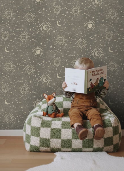 Kindertapete mit Motiven von Sonne, Mond und Sternen in einem Kinderzimmer mit einem Kind, das auf einem Sitzsack liest.
