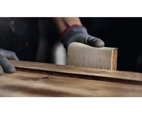 Eine Person schleift ein Holzbrett mit einem Schleifklotz.