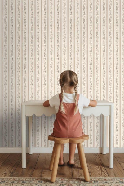Papiertapete mit vertikalem Streifen- und Blumenmuster in einem hellen Kinderzimmer mit weißem Schreibtisch und Holzschemel.