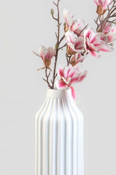 Künstlicher Magnolienzweig mit rosa-weißen Blüten in einer weißen, gerippten Vase aus Keramik.
