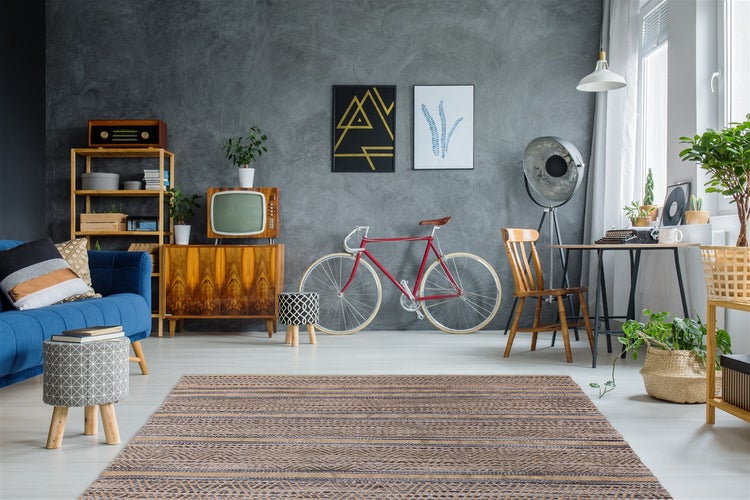 Modernes Wohnzimmer mit grauer Wand, blauem Sofa, Rennrad als Dekoration, Holzmöbeln und einem gemusterten Webteppich im Industriestil.