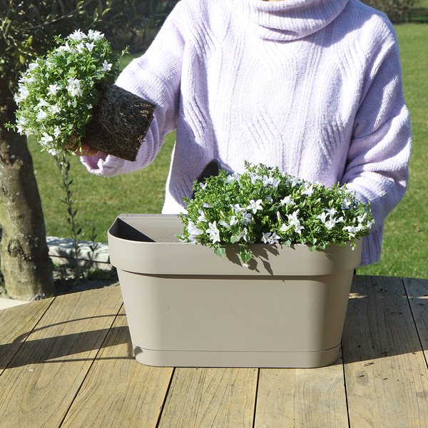 Frau pflanzt Blumen in einen Pflanzkasten auf einem Holztisch.