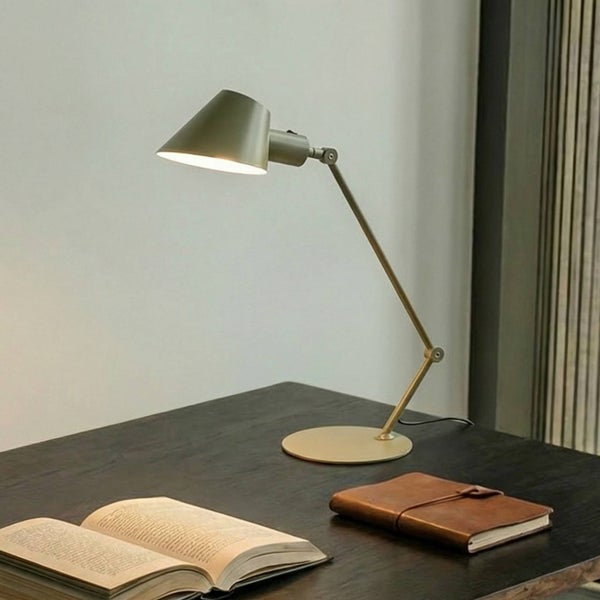 Schreibtischszene mit einer verstellbaren Schreibtischlampe, einem Notizbuch und einem aufgeschlagenen Buch