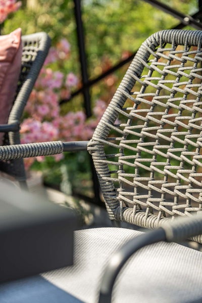 Nahaufnahme eines Gartenstuhls mit Seilgeflecht an der Rückenlehne und Armlehne sowie einem Sitzkissen.