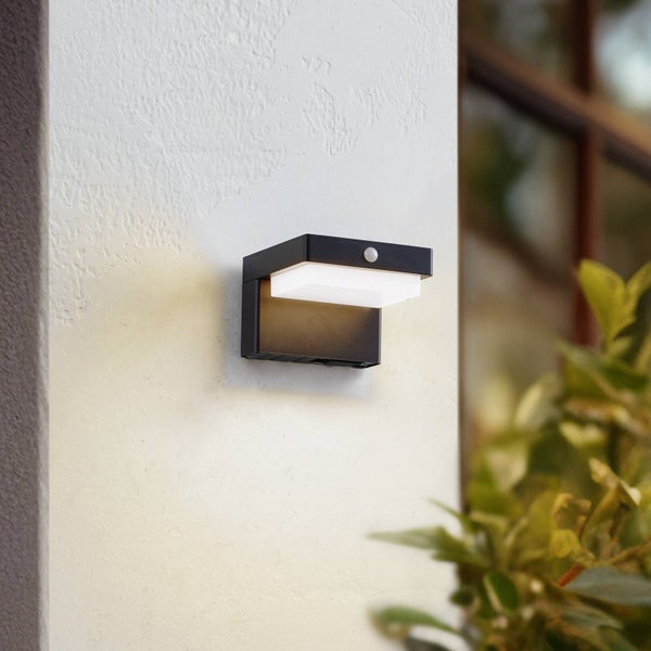 Moderne schwarze Außen-LED-Wandleuchte mit Bewegungsmelder an einer strukturierten Wand, nach unten leuchtend.