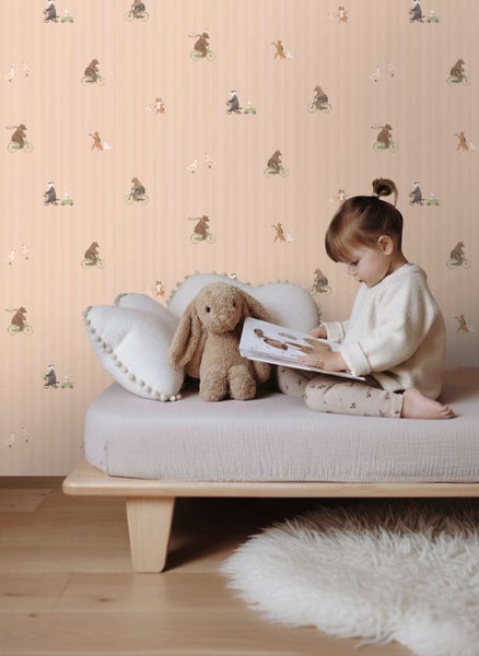 Kindertapete mit Tiermotiven an der Wand hinter einem Kind, das auf einem Bett mit Stofftier liest.