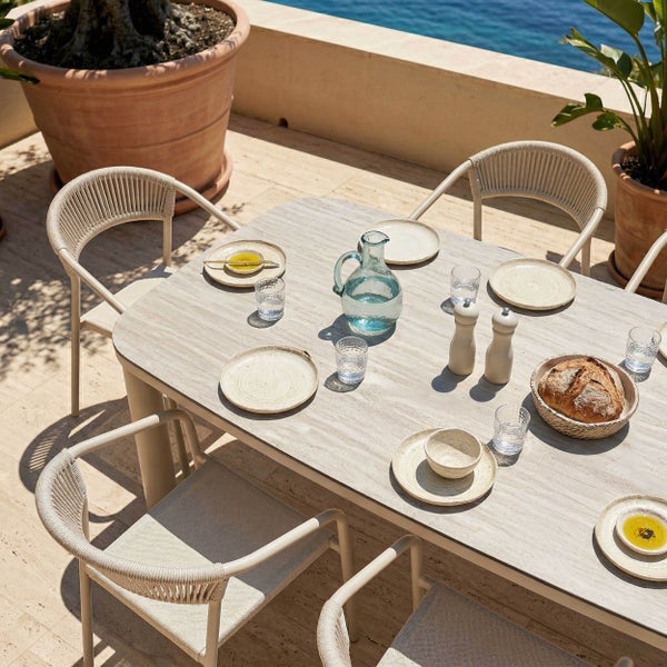 Gedeckter Gartentisch mit Platte in Steinoptik und Gartenstühle mit Rückenlehne aus Seilgeflecht auf einer hellen Terrasse.