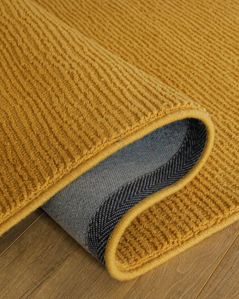 Senfgelber gerippter Teppich mit weicher Struktur und sichtbarer Rückseite.