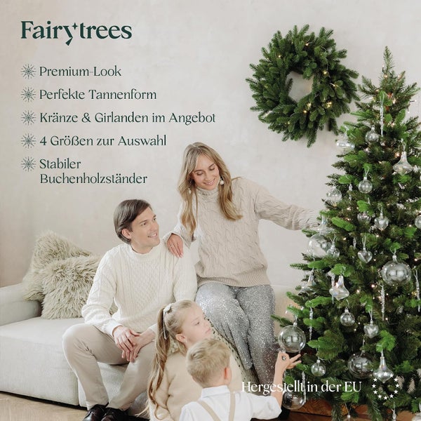 Familie schmückt einen Fairy Trees Weihnachtsbaum mit Premium Optik und Buchenholzständer sowie einem beleuchteten Weihnachtskranz an der Wand.