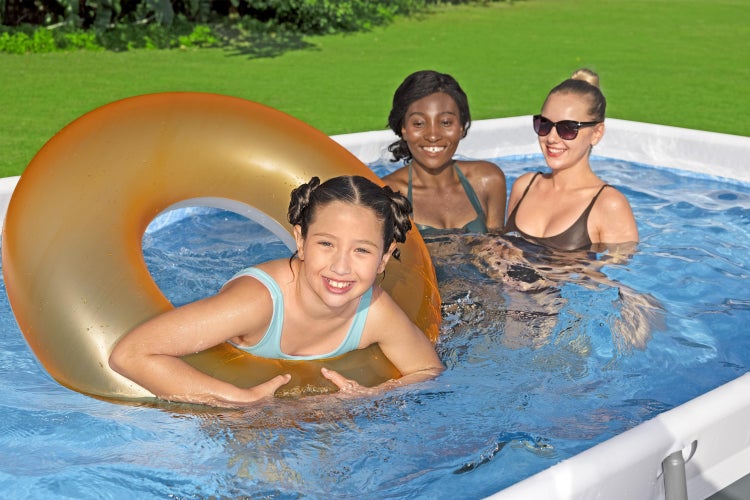 Mädchen mit Schwimmreifen und zwei Frauen in einem rechteckigen Aufstellpool im Garten auf einer grünen Wiese.