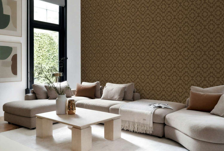 Wohnzimmer mit einer Wand, die mit einer Tapete mit geometrischem Muster tapeziert ist, davor steht ein helles Sofa mit dekorativen Kissen.
