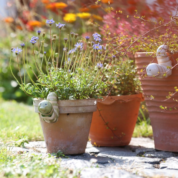 Blumen in Blumentöpfen mit dekorativen Keramikfiguren im Garten.