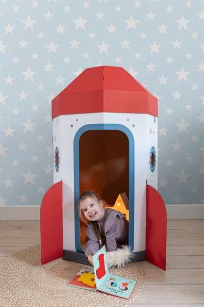 Mädchen spielt in einer Papprakete im Kinderzimmer