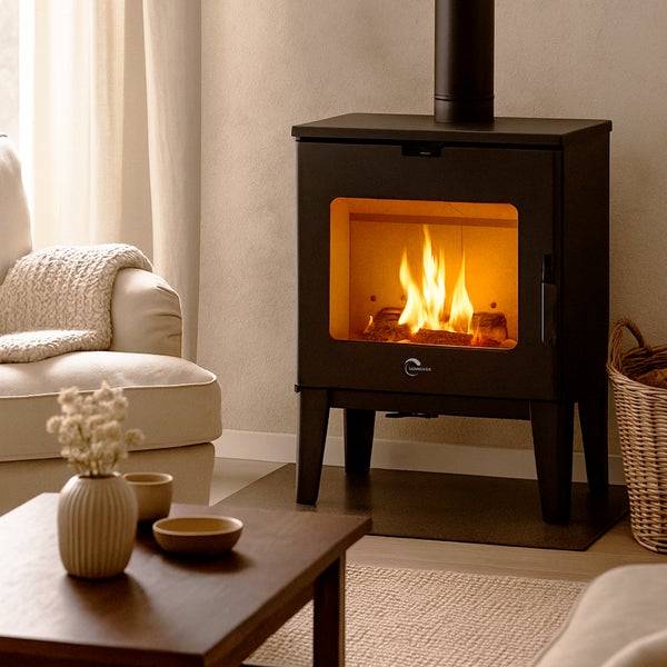 Schwarzer Sannover Kaminofen mit Sannover Logo im hellen Wohnzimmer mit Sessel und Tisch. Gemütliche Atmosphäre durch brennendes Feuer.