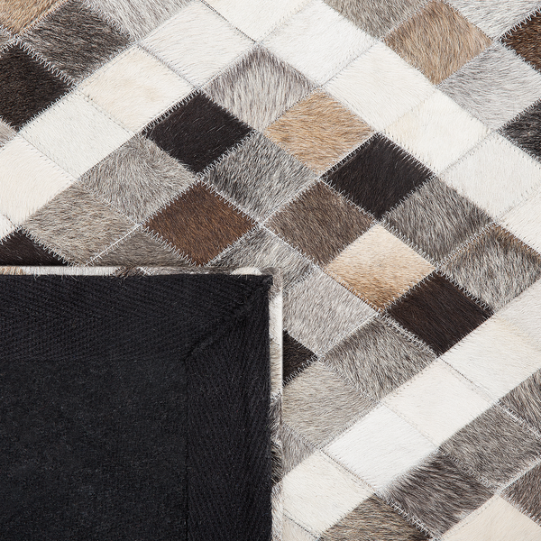 Patchwork-Teppich aus quadratischen Kuhfellstücken mit Zickzack-Nähten und umgeklappter Ecke mit dunkler Rückseite.