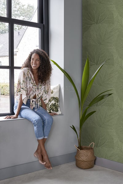 Frau sitzt am Fenster mit Blättermuster-Tapete