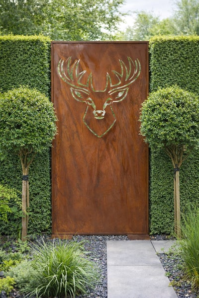 Garten-Sichtschutzwand aus Metall mit Edelrost-Optik und Hirsch-Motiv, platziert zwischen Hecken in einer Gartenlandschaft.