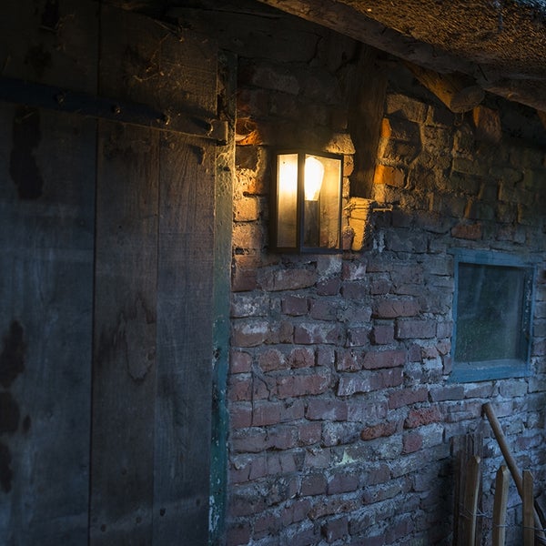 Rechteckige Außenwandleuchte mit warmem Licht an einer rustikalen Ziegelwand neben einer Holztür.