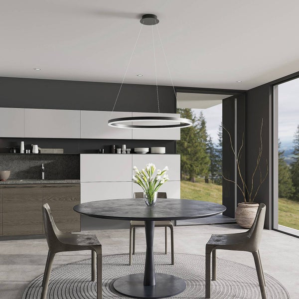 Moderne Küche mit kreisförmiger LED-Pendelleuchte über einem runden Esstisch, minimalistische Einrichtung und Blick ins Grüne.