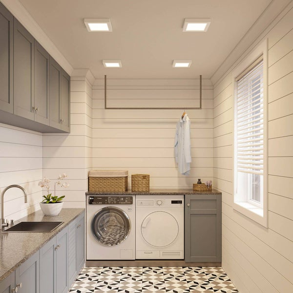 Ein moderner Hauswirtschaftsraum mit vier quadratischen LED-Einbauleuchten an der Decke, Waschmaschine, Trockner und grauen Schränken.