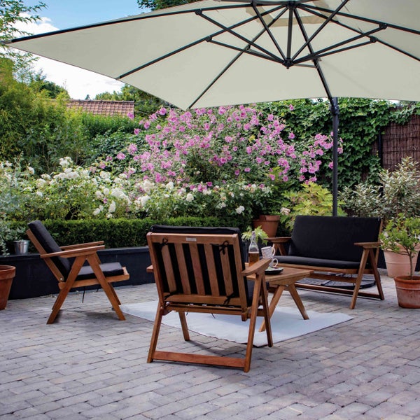 Gartengarnitur aus Holz mit dunklen Polstern, bestehend aus Sesseln, Sofa und Tisch, unter einem großen hellen Sonnenschirm auf einer Terrasse.