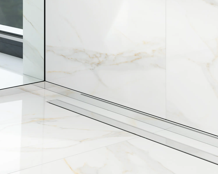 Duschrinne aus Edelstahl bodeneben eingebaut in einen Boden und eine Wand mit Fliesen in Marmoroptik.