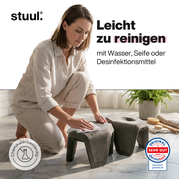 Eine Frau reinigt in einem hellen Badezimmer einen stuul Toilettenhocker. Er ist chemikalienbeständig und dermatologisch sehr gut bewertet. stuul Logo.
