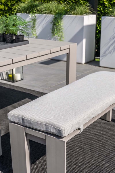 Moderne Gartenbank mit gepolstertem Sitzkissen aus Stoff und passendem Gartentisch aus Aluminium auf einer Terrasse.
