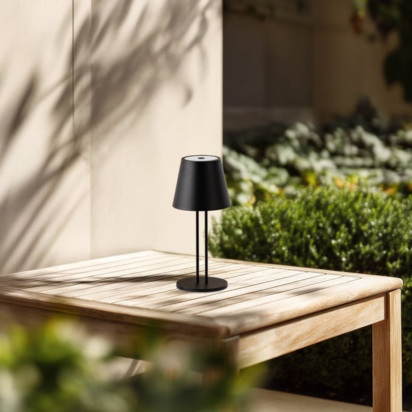 Tragbare schwarze LED-Tischleuchte mit konischem Schirm auf einem hölzernen Gartentisch im hellen, modernen Außenbereich.