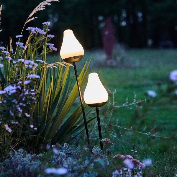Zwei Gartenleuchten auf Spießen in einer abendlichen Gartenszene