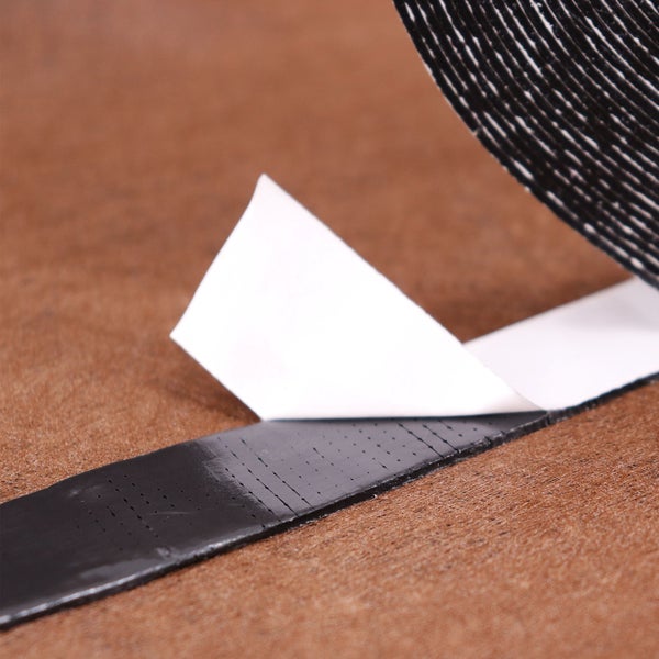 Nahaufnahme eines schwarzen Klettbandes mit weißer Schutzfolie auf einer braunen Oberfläche