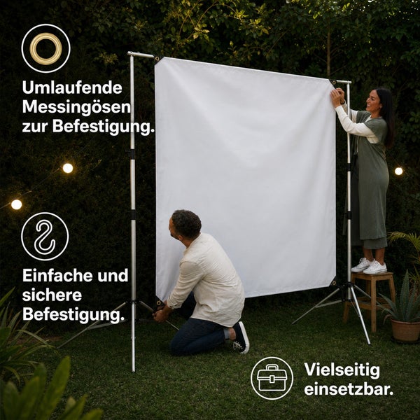 Zwei Personen bauen eine weiße Leinwand mit umlaufenden Messingösen für die Außenanwendung im Garten auf einem Metallstativ auf.