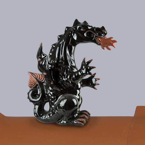 Schwarzer feuerspeiender Drache aus glasierter Keramik als Firstfigur auf einem Firstziegel.