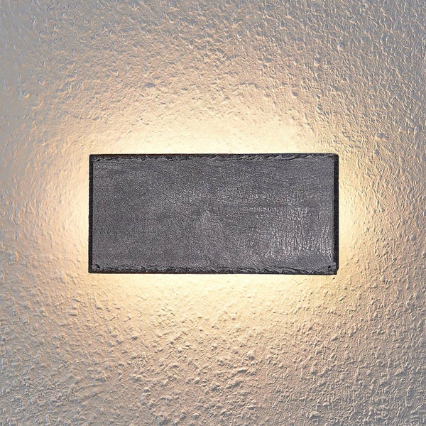 Rechteckige Wandleuchte in Schieferoptik mit Up- und Downlight-Effekt auf einer strukturierten Wand.