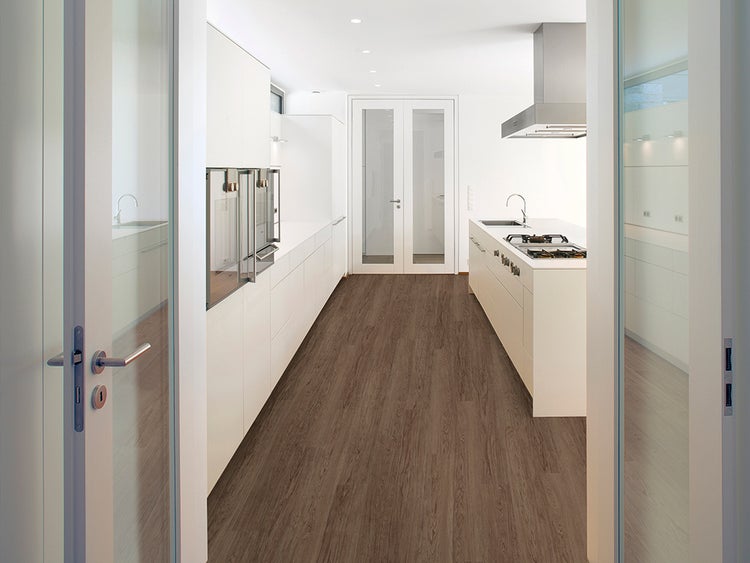 Moderne, helle Küche mit Schränken und Boden in Holzoptik, gesehen durch eine Türöffnung.