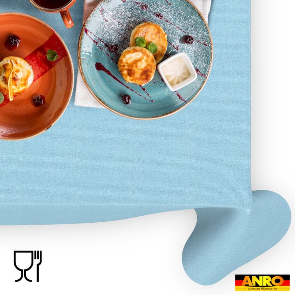Hellblaue Tischdecke aus Stoff in einer Frühstücksszene mit Tellern und Speisen. Lebensmittelecht. ANRO Deutsche Manufaktur Logo.
